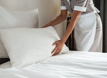 Camarera tendiendo una cama con ropa de cama blanca