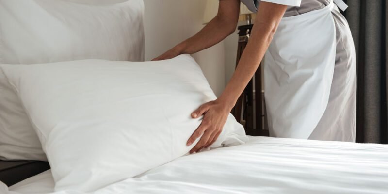 Camarera tendiendo una cama con ropa de cama blanca