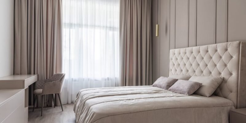 Cama de hotel con cabecera tapizada y ropa de cama blanca