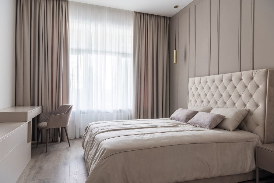 Cama de hotel con cabecera tapizada y ropa de cama blanca